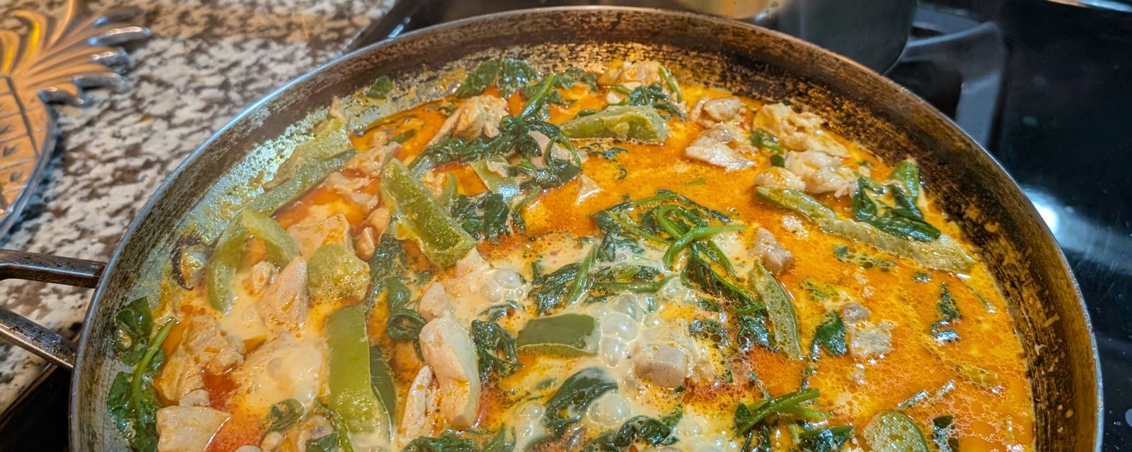 A pan of chicken and greens simmering in a red coconut curry on the stove
