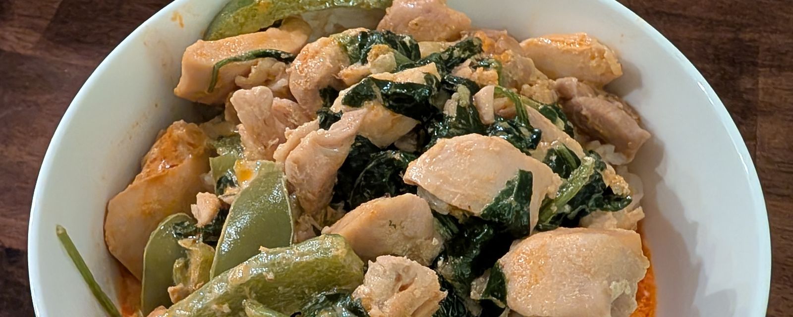 A bowl of chicken and greens in a red coconut curry over rice