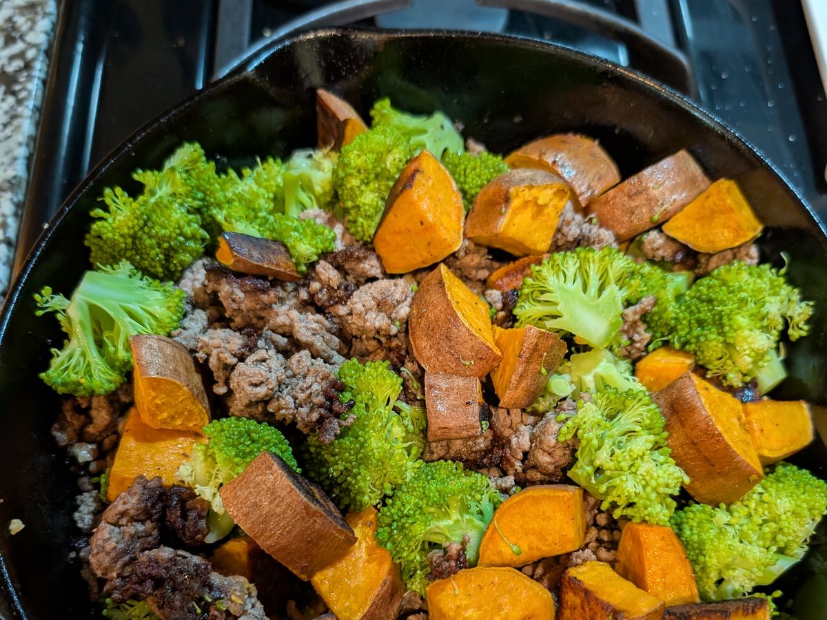 A cast-iron skillet of ground beef, roasted sweet potato, and broccoli