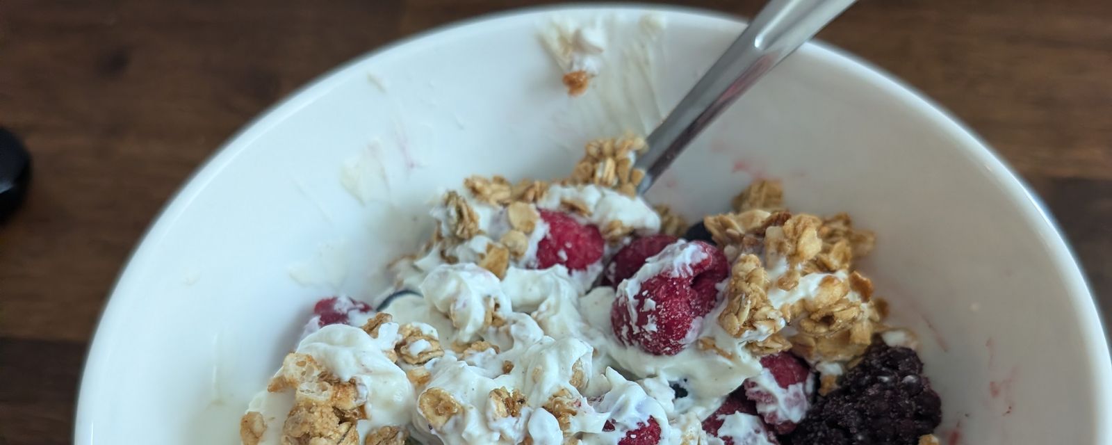 A bowl of Greek yogurt with raspberries, blackberries, and granola on a wooden table