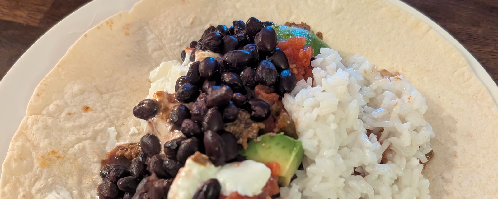 A tortilla topped with black beans, rice, avocado, salsa, and crumbled cheese