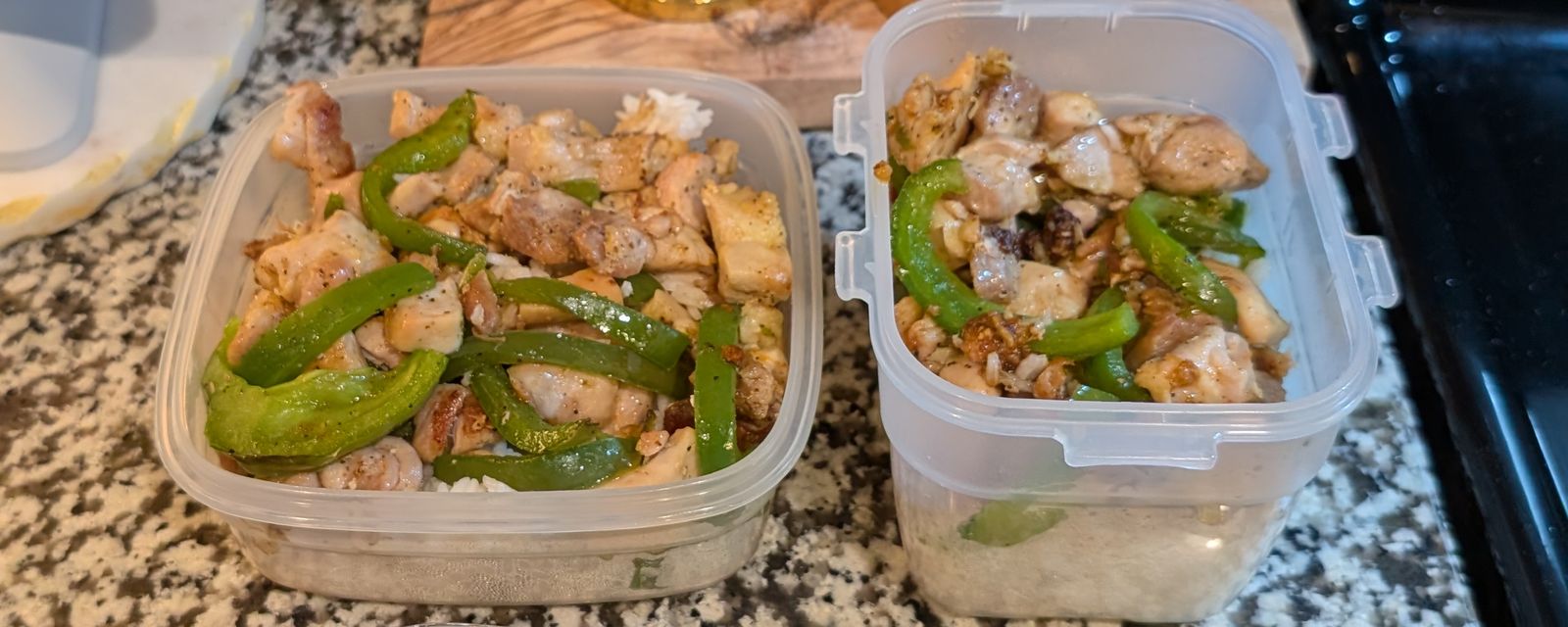 Two glass meal-prep containers of chicken, peppers, and rice on a kitchen counter