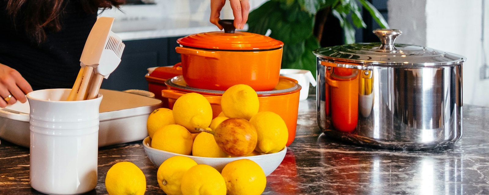 A marble kitchen counter with an orange Dutch oven, a bowl of lemons and fresh greens ready for the week's cooking